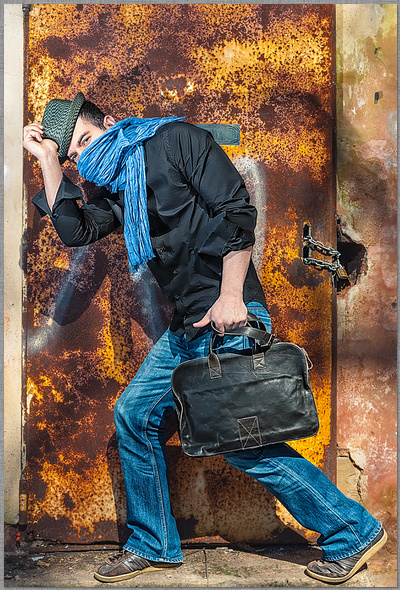 Person mit große Ledertasche und blauem Schaal vor einer rostigen Tür in orange und blau dirk schmitz